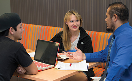 Advisor talking to two students while they work in a desk