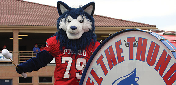 Wolfie holding a drumstick next to a giant kick drum