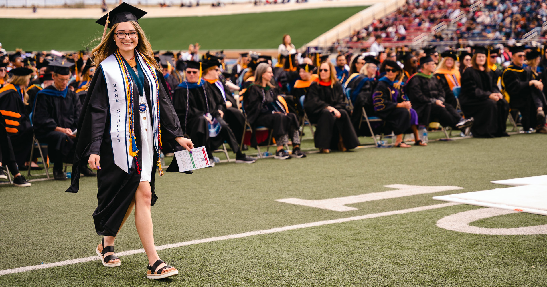 female graduate walking with crowd behind her