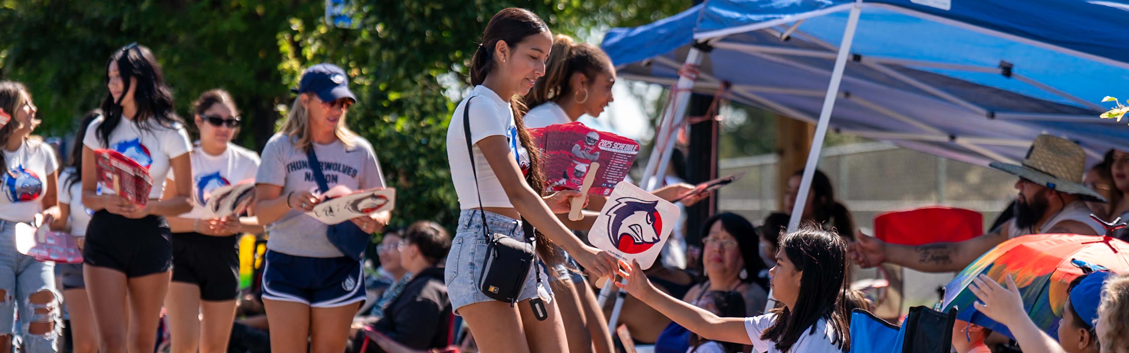 students and staff handing out fans to community members at the Fiesta Day Parade