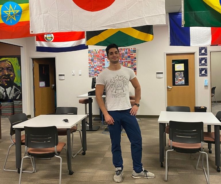 International student standing among various flags of different countries in the Center for International Programs and Inclusive Excellence