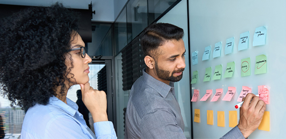 two business professionals brainstorming on a white board with sticky notes