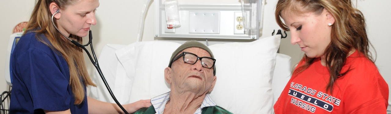 Nursing students attending older person in hospital bed
