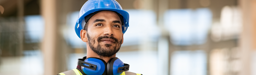 Man smiling with a hard hat on in front of a building
