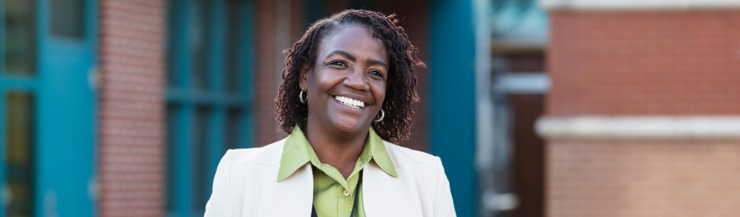 Woman smiling with a walkie talkie in front of a school building