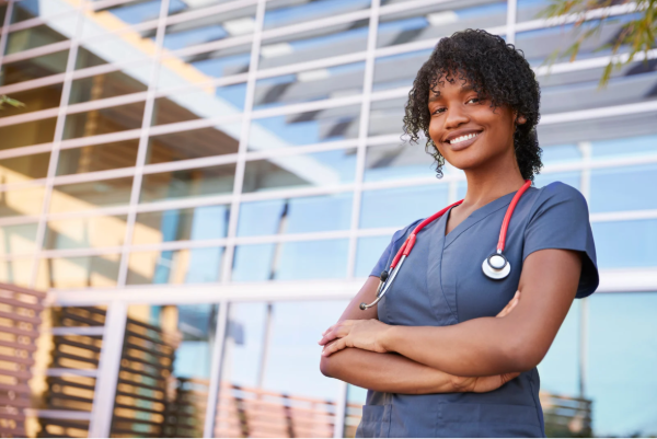 Woman smiling in scrubs in front of a building with a stethoscope