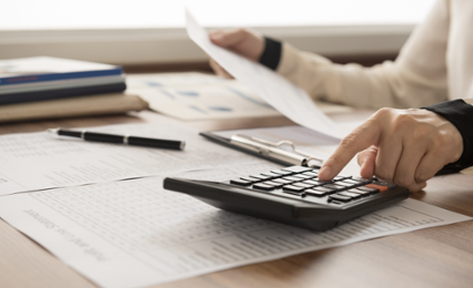 Hands typing buttons on calculator with paperwork